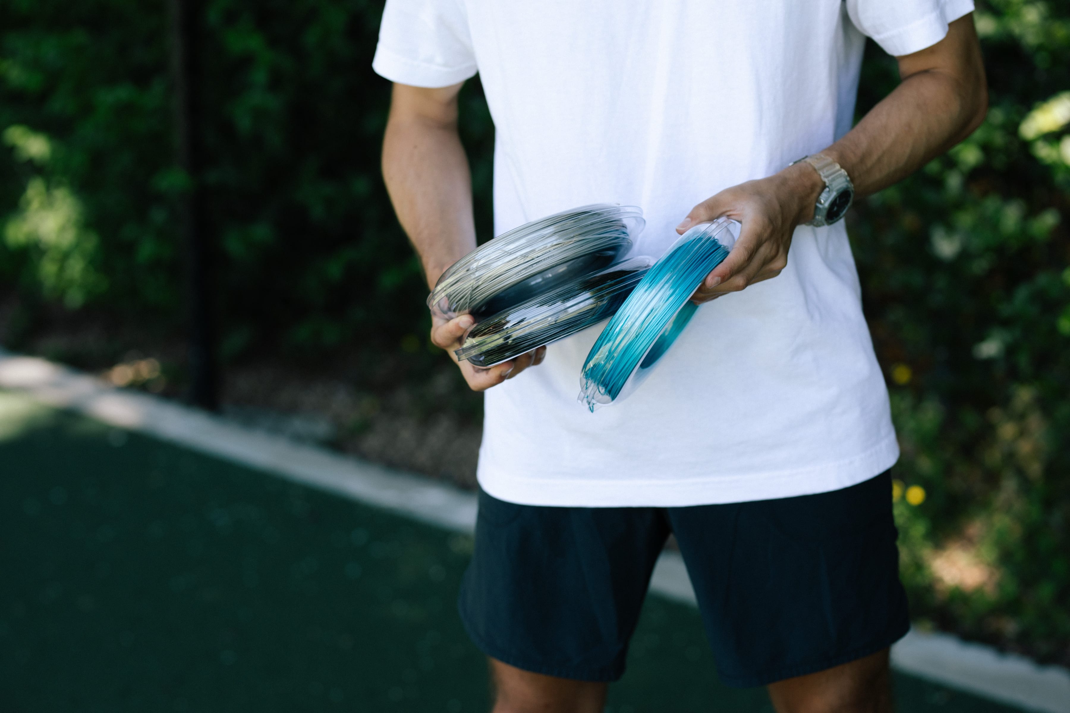 Reels of reString racket string held in hand beside a tennis court