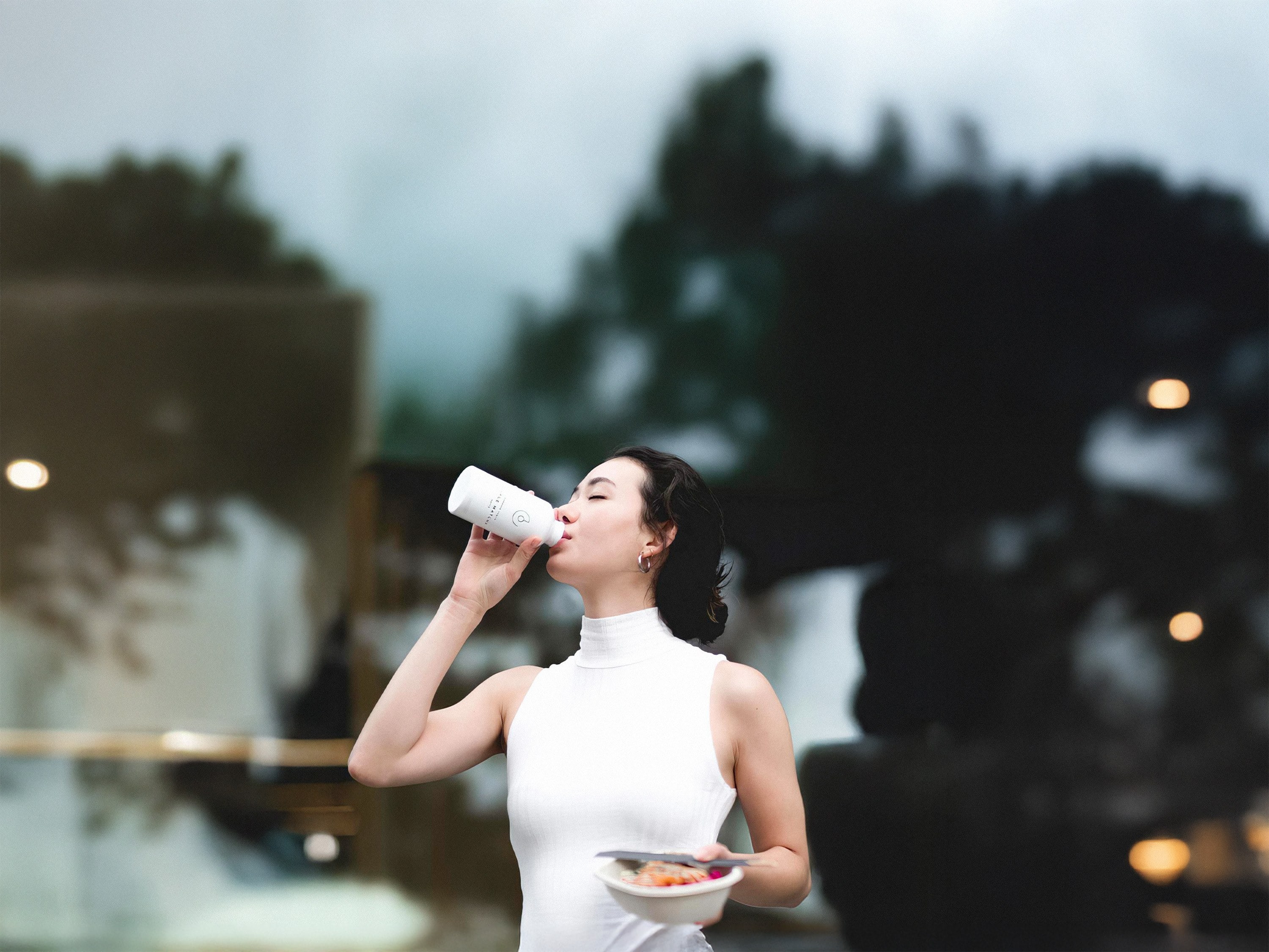 A woman drinking from a white bottle on an evening street