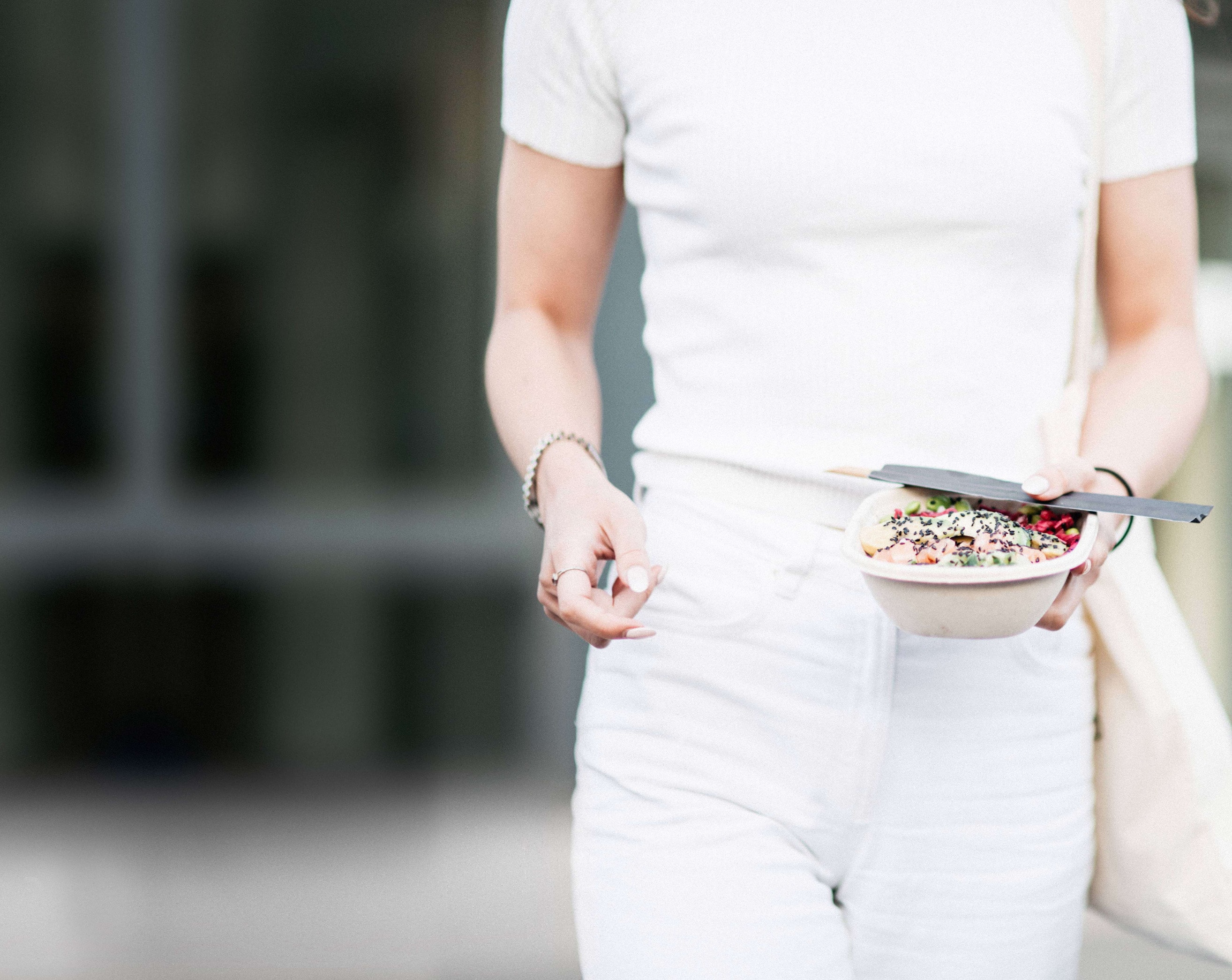 A woman in white carrying a bowl of food along a city street