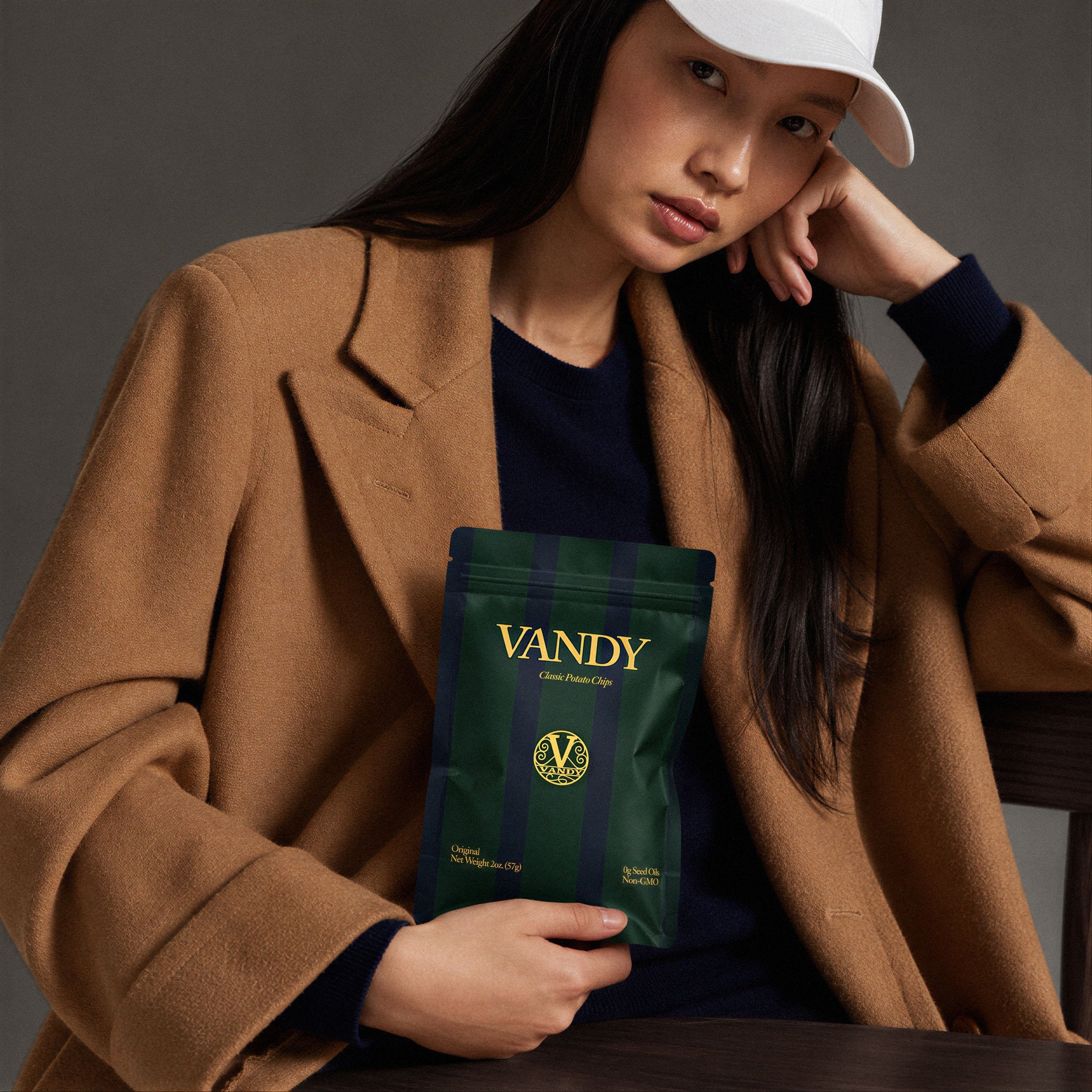 A woman in a camel coat holding a green VANDY crisps pouch